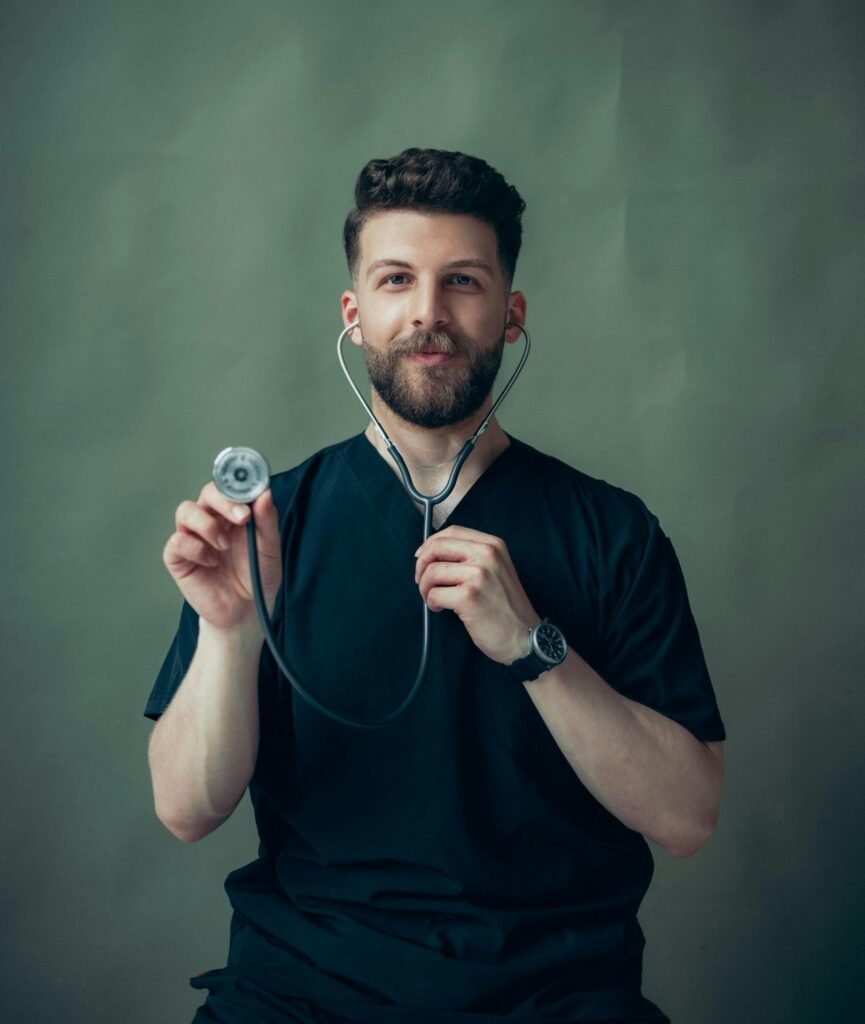 Portrait of a young male doctor with a stethoscope, wearing a black t-shirt.